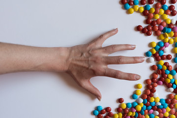 A hand pulls for colorful chocolate coated candy on white background. Unhealthy nutrition concept