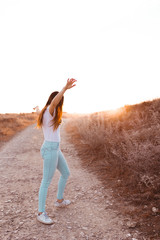 young woman raising arms at sunset in the field