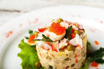 Salad Olivier with red caviar, chicken meat and beluga on a white plate. Traditional Russian cuisine, meat salad close-up and copy space.
