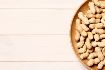  Dry peanuts in a wooden bowl on a white wooden background. Place for text. Top view.