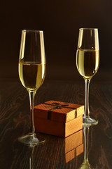 Two glass with white wine and gift box on mirror table. Celebrities composition. Selective focus.