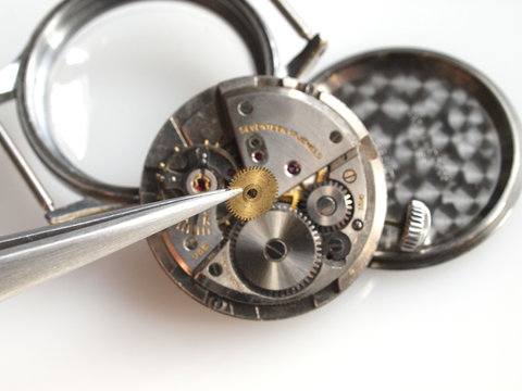 close up of watchmaker repairing old mechanical watch caliber taking small gear with tweezers