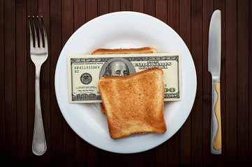 Conceptual photo. Sandwich with one hundred dollar bills. On a white plate. Near fork and knife. Top view. - 248518689