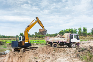 Yellow excavator machine loading soil into a dump truck at construction site