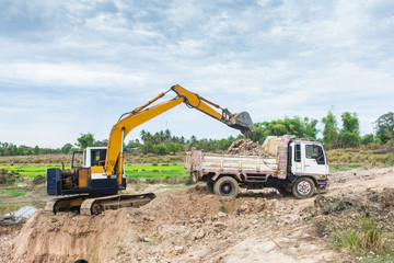 Fototapeta premium Yellow excavator machine loading soil into a dump truck at construction site