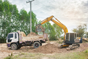 Yellow excavator machine loading soil into a dump truck at construction site