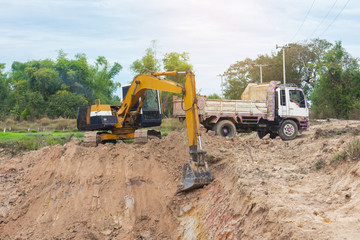 Fototapeta premium Yellow excavator machine loading soil into a dump truck at construction site