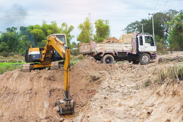 Obraz premium Yellow excavator machine loading soil into a dump truck at construction site