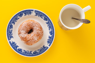 A mug with plant based milk and a plate with sugar coated doughnut, on yellow background.