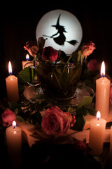 Enchanted tea surrounded by burning candles, with flowers in a cup. Silhouette of a witch on the background of a bright moon.