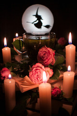 Enchanted tea surrounded by burning candles, with flowers in a cup. Silhouette of a witch on the...