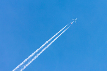 Plane flying high in clear blue sky leaving long white trail