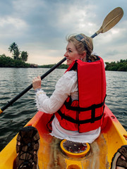 Caucasian woman, mod 40's kayaking through the cambodian Jungle on the River Kong, wearing red life...