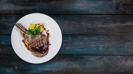 Rib-eye steak with corn rotating on a white plate. Top view on a wooden background. Copy space for your text.
