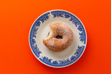 A doughnut coated with sugar on white round plate with decoration , on blue background.