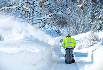 A man clears snow from the sidewalks with snowblower in the countryside
