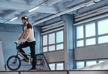 Fototapeta na wymiar Professional BMX rider in protective helmet getting ready to jump in a skatepark indoors