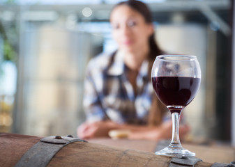 girl looking at glass of red wine standing on wooden barrel in winery