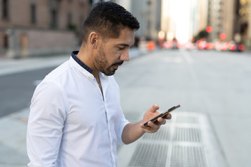 Young Latino Hispanic man in city walking texting on cell phone