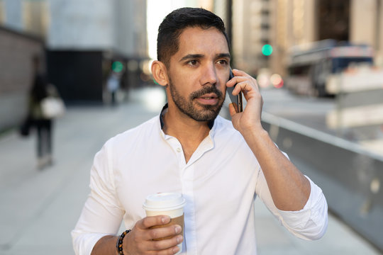 Young Latino Hispanic man in city walking talking on cell phone