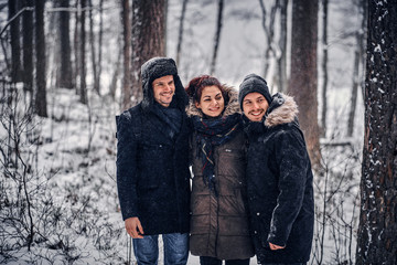 A group of happy friends stand next to each other and look at the camera in the midst of a snowy forest