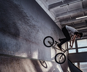 Professional BMX rider in protective helmet performing tricks in skatepark indoors