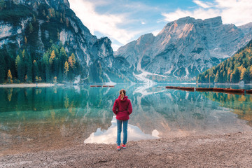 Woman in red jacket is standing on the coast of Braies lake at sunrise in autumn. Dolomites, Italy....