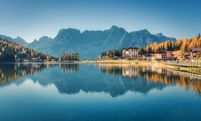 Fototapeta na wymiar Beautiful famous Misurina lake at sunset in autumn in Dolomites, Italy. Landscape with lake, mountains, blue sky reflected in water, buildings, colorful forest in italian alps. Travel and nature