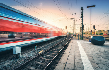 Red high speed train in motion on the railway station at colorful sunset. Blurred modern intercity...