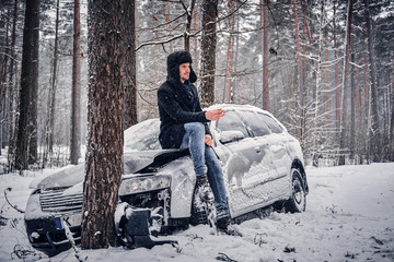 The car got into a skid and crashed into a tree on a snowy road. A frustrated driver sits on the...