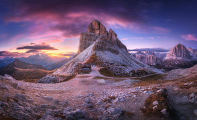 Mountain pass and beautiful sky with colorful clouds at sunset. Amazing panoramic landscape with rocks, mountain peaks, stones, trails, buildings, trees on hills at dusk. Autumn in Dolomites, Italy - obrazy, fototapety, plakaty