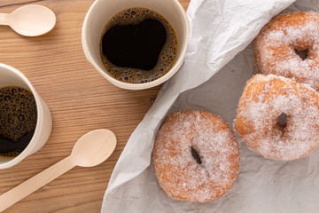 Sugar coated doughnuts on crumpled paper with two reusable cups of coffee , on wooden background.