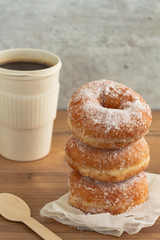 A stack of sugar coated doughnuts on crumpled paper with a hot cup of coffee , on wooden background.