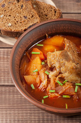 Traditional Ukrainian borsch with meat on the edge, in a brown clay bowl, on a wooden background.
