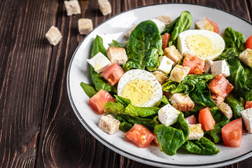 Fresh vegetable salad with tomatoes, spinach, bread crumbs, egg and feta. Healthy food. Dietary dinner or lunch menu. Salad plate on the table.