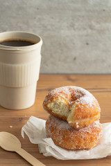 A stack of sugar coated doughnuts on crumpled paper with a hot cup of coffee , on wooden background.