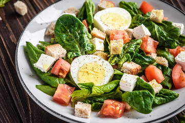 Fresh vegetable salad with tomatoes, spinach, bread crumbs, egg and feta. Healthy food. Dietary dinner or lunch menu. Salad plate on the table.