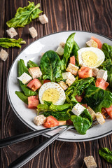 Fresh vegetable salad with tomatoes, spinach, bread crumbs, egg and feta. Healthy food. Dietary dinner or lunch menu. Salad plate on the table.