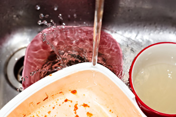 Water running over dirty dishes in metal sink.