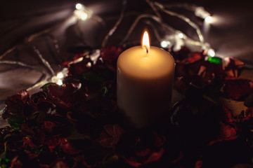 Dark romantic background. Candle decorated with flowers and lights.