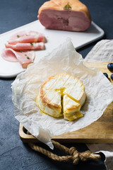 Italian intipasto - baked Camembert with blueberries and ham. Dark background, side view, space for text