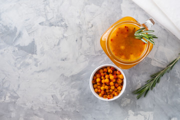 Colorful hot sea buckthorn tea with rosemary and fresh sea buckthorn berries on a grey table. Vitamin drink.