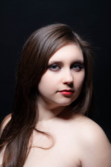 Fototapeta premium Beautiful gray-eyed brown-haired woman with red lips and bared shoulders against black background. Closeup studio portrait
