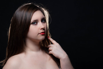 Beautiful gray-eyed brown-haired woman with red lips and bared shoulders against black background. Closeup studio portrait