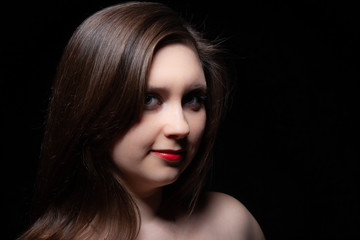 Fototapeta premium Beautiful gray-eyed brown-haired woman with red lips and bared shoulders against black background. Closeup studio portrait