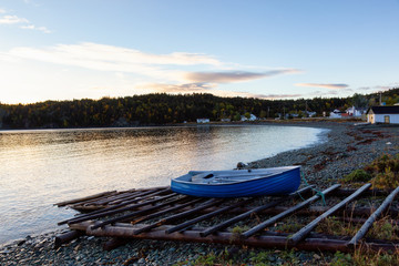 Obraz premium Wooden boat laying by the Atlantic Ocean Shore during a vibrant sunrise. Taken in Beachside, Newfoundland, Canada.