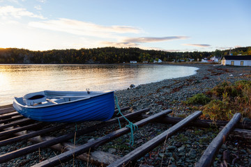Obraz premium Wooden boat laying by the Atlantic Ocean Shore during a vibrant sunrise. Taken in Beachside, Newfoundland, Canada.