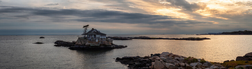 Panoramic seascape view of a beautiful home on a rocky island during a vibrant sunset. Taken on the Atlantic Ocean in New Haven, Connecticut, United States. - obrazy, fototapety, plakaty