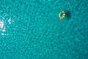 Fototapeta na wymiar Aerial view of slim woman swimming on the swim ring donut in the transparent turquoise sea in Seychelles. Summer seascape with girl, beautiful waves, colorful water. Top view from drone