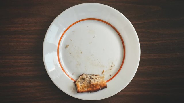 Eating of piece of apple pie bite by bite on white plate on brown wooden table top view stop motion seamless